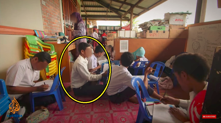 ferdi at school sitting on floor work on chair. Screenshot from video.png  848×473