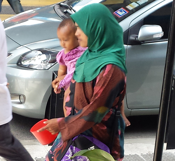 Woman carrying a child around while begging near Masjid Jamek