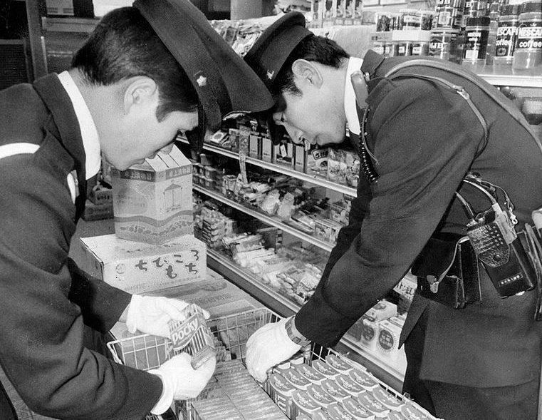 Police officers check Glico products at a supermarket in December 1984 in Osaka, Japan. Img from Atlas Obscura.