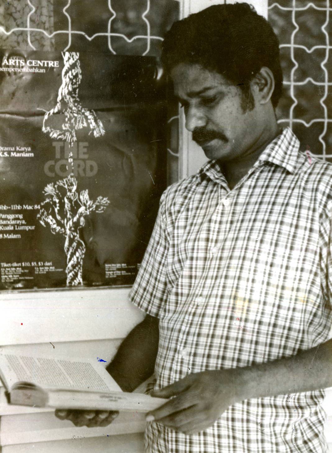 K.S. Maniam standing before a poster of his play, The Cord, in 1984. Img from The Star