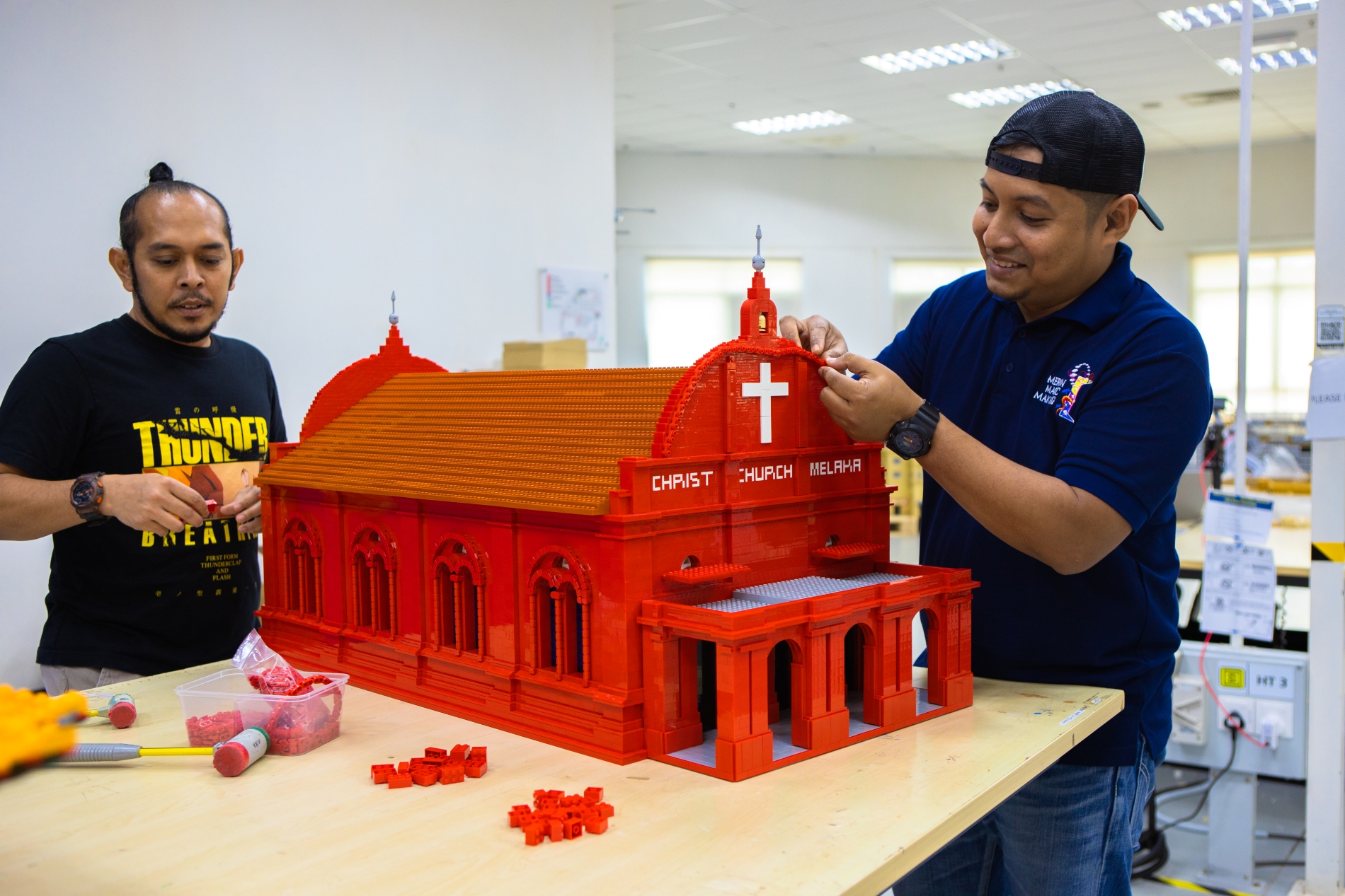 2 LEGO builders building a LEGO model of Malacca's Christ Church.