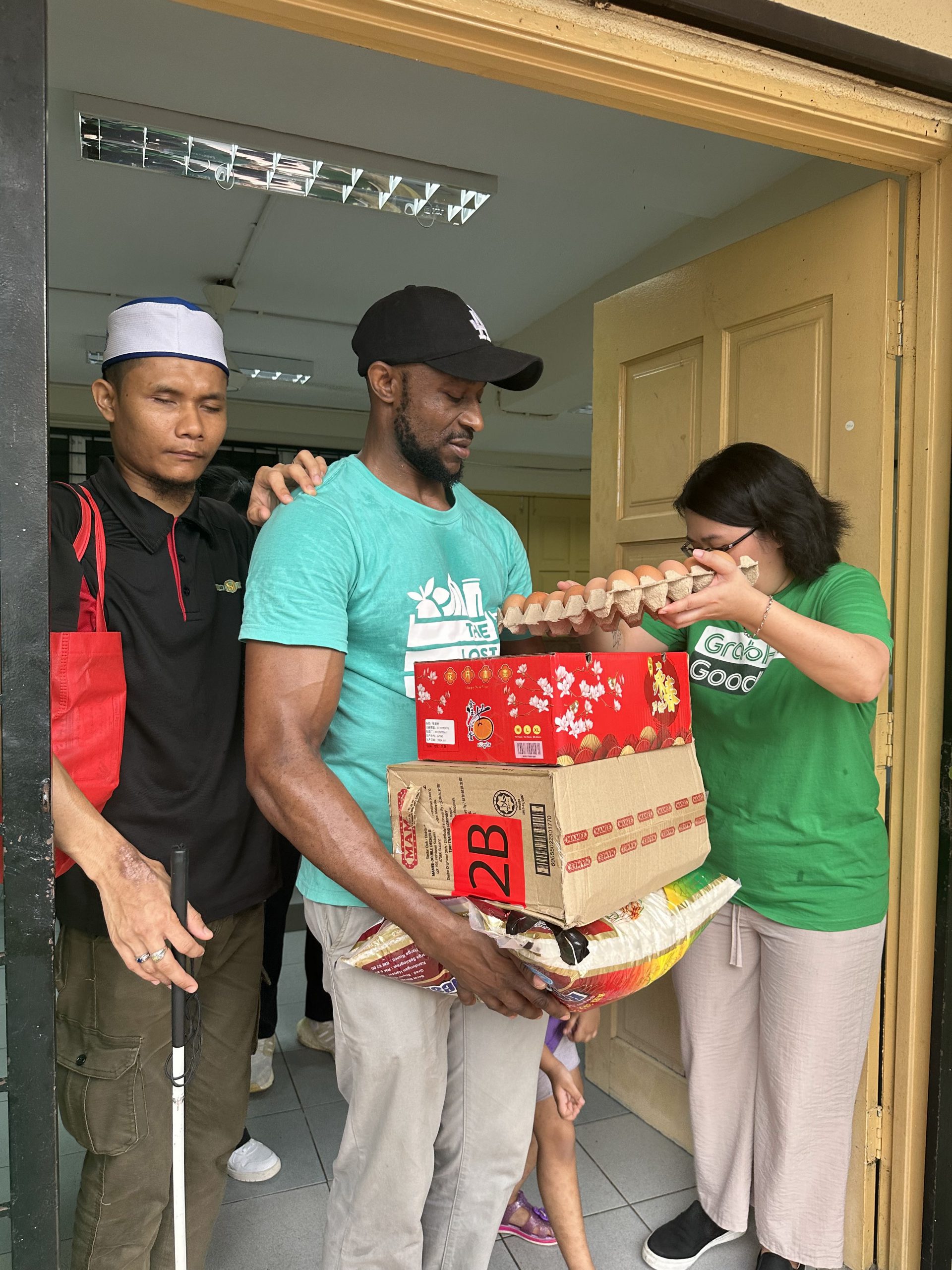 A member of The Lost Food Project assisting a visually-impaired resident by carrying the essential items that he had received from the #GongXiMakan For All initiative.